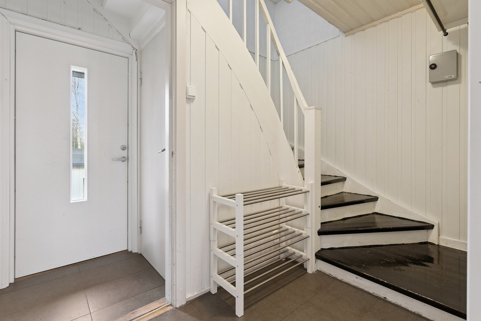 Entré med flislagt gulv og trapp som leder opp til andre etasje og ned til underetasjen. Galleribilde