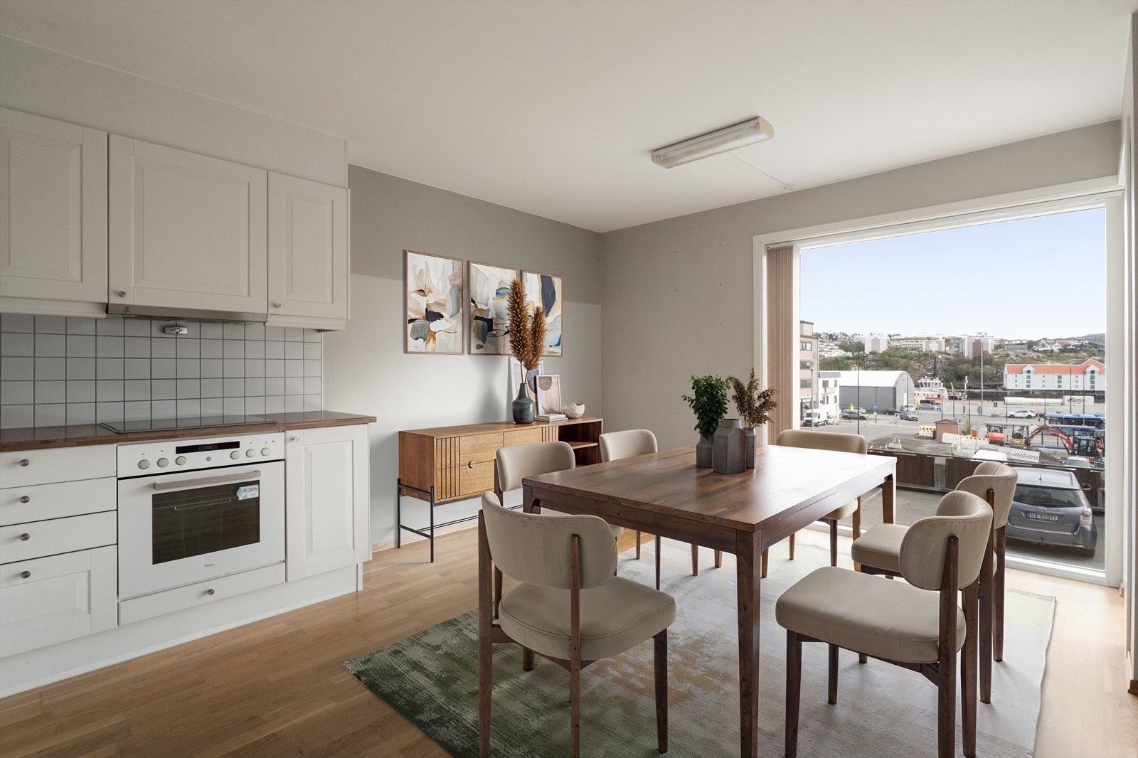 Kjøkkeninnredningen har profilerte fronter, integrerte hvitevarer og benkeplate i laminat. Foran de store vinduene er det montert lamellgardiner. (Bildet er digitalt møblert) Galleribilde