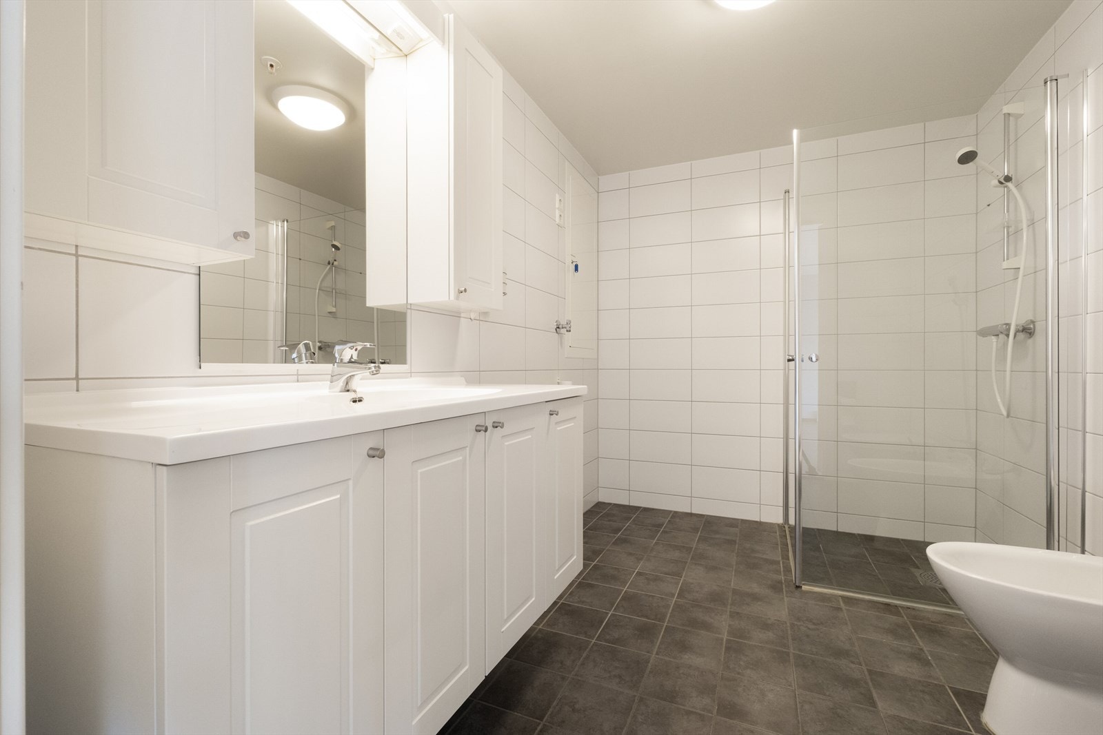 Badet har flislagte overflater og elektrisk gulvvarme, samt dusjhjørne med glassdører og heldekkende servant. Galleribilde