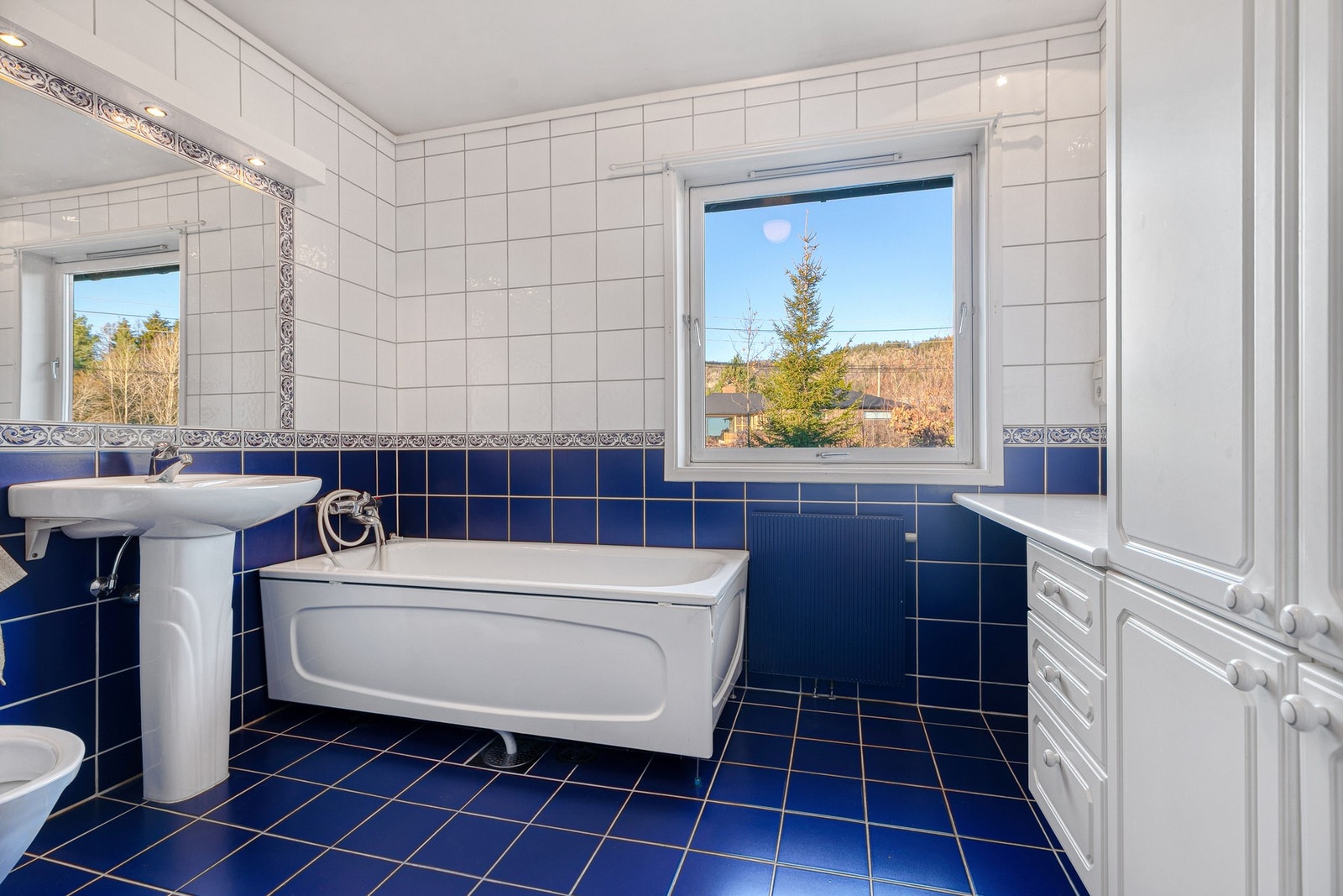 Eldre bad fra rundt 1993 har god størrelse og innredning med toalett, servant, skapinnredning og et frittstående badekar Galleribilde