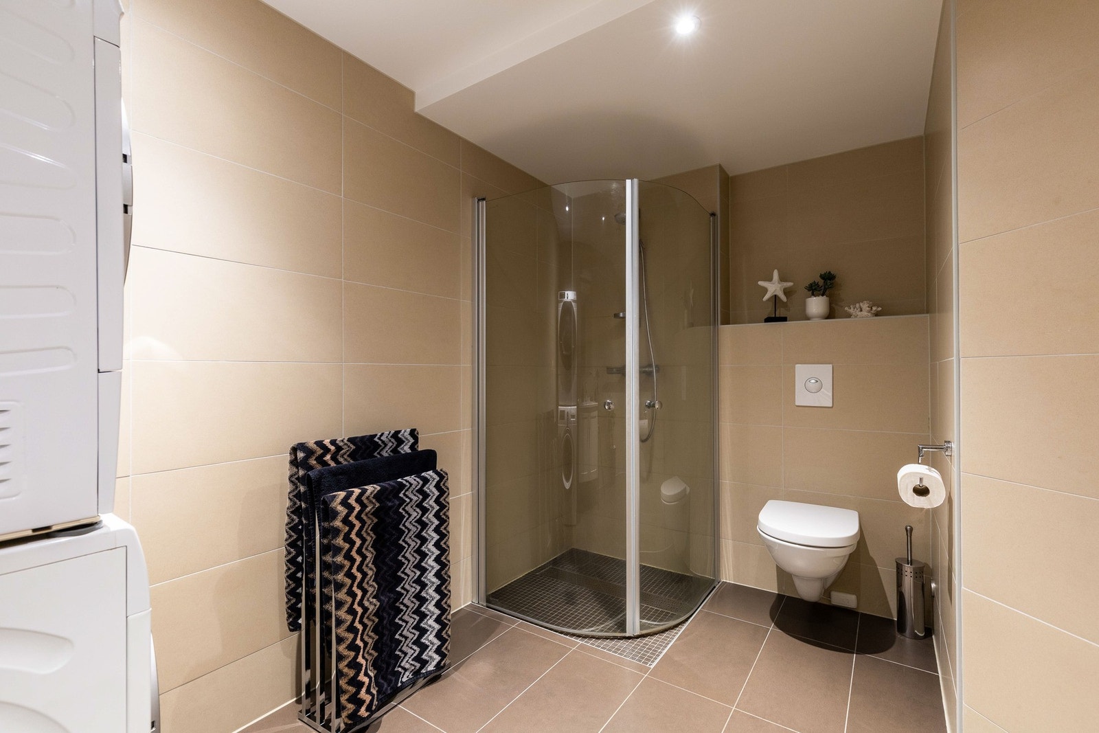 Det er innredet med et praktisk dusjhjørne som sørger for effektiv plassutnyttelse, samt opplegg for både vaskemaskin og tørketrommel. Galleribilde