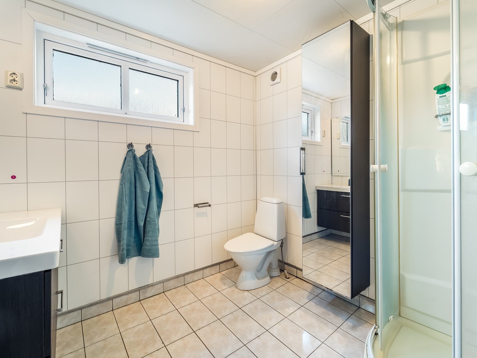 Bad med fliser på gulv og baderomsplater på vegg. Innredet med baderomsinnredning, toalett og dusjkabinett. Varmekabler i gulv. Galleribilde