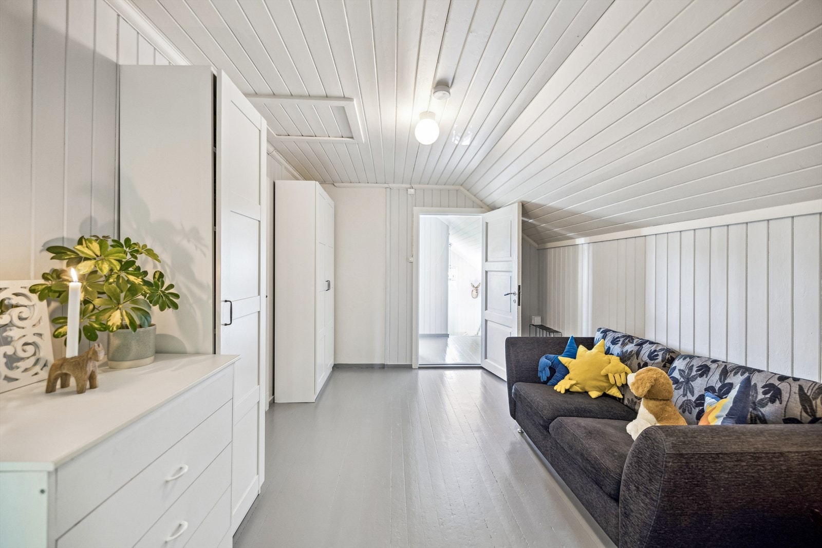 Den lyse stuen i loftsetasjen er et sjarmerende rom med malt tregulv, hvitmalte vegger og noe skråhimling. Galleribilde