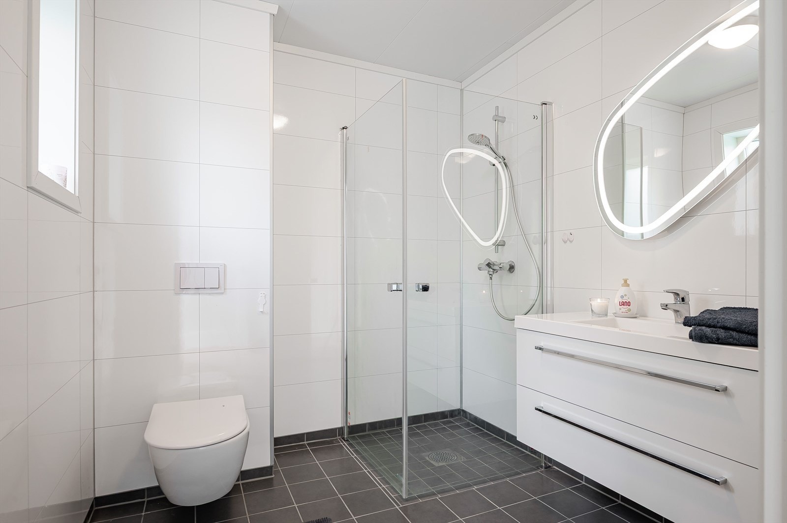 Badet inneholder vegghengt toalett, hjørnedusj og sevant med speil. Galleribilde