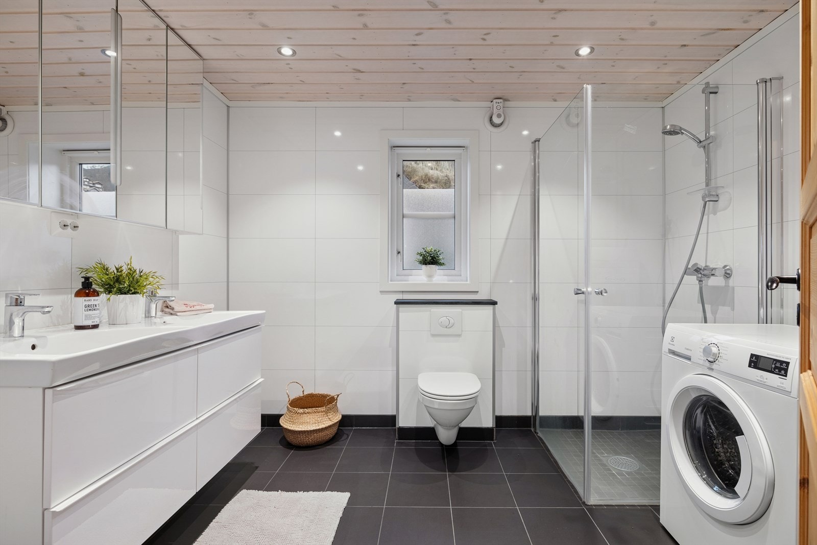 Romslig og stilrent baderom med dusjhjørne, vegghengt toalett og stor servant med god oppbevaringsplass. Praktisk løsning med opplegg for vaskemaskin og gjennomført design. Galleribilde