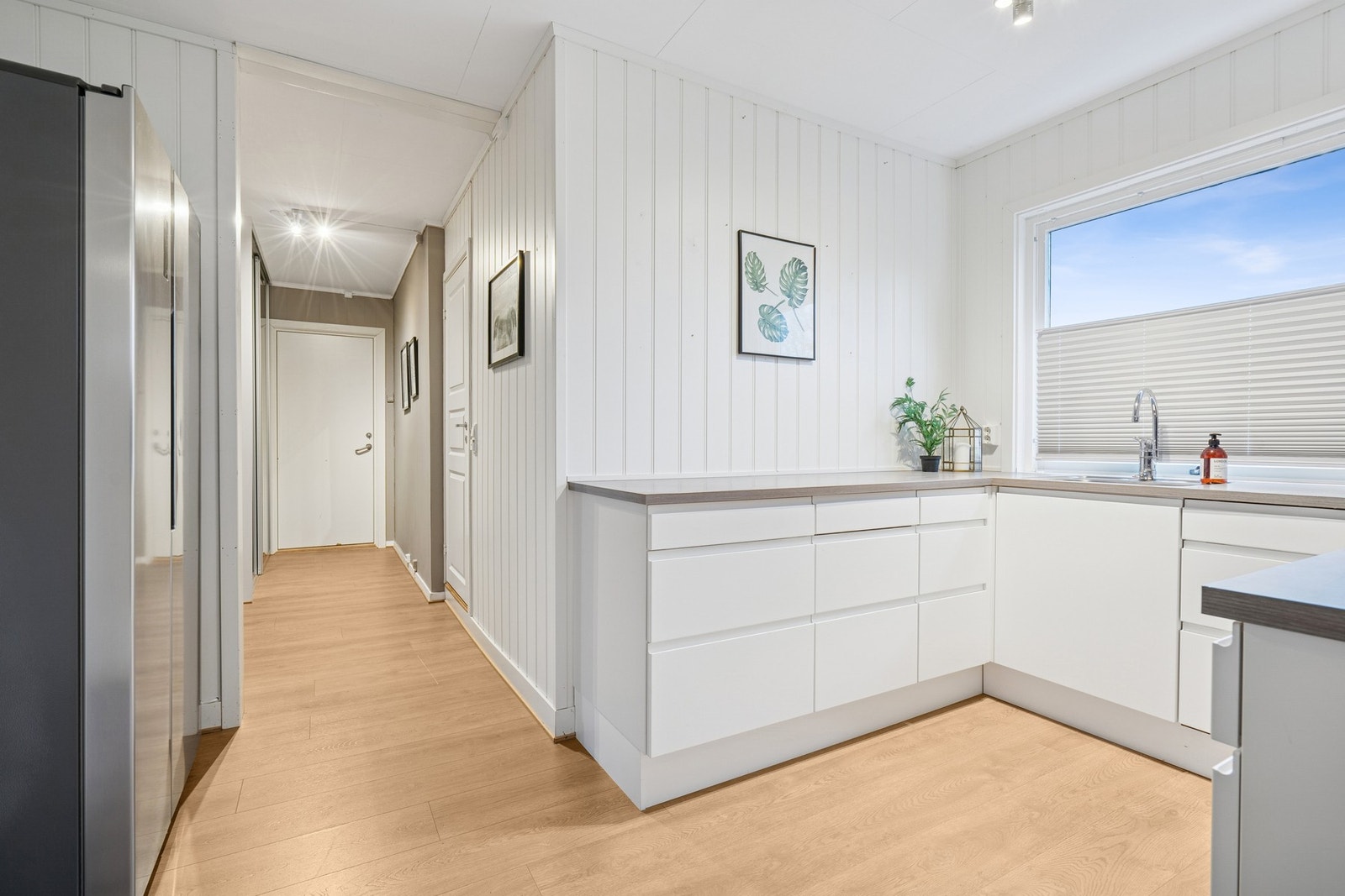 Kjøkkeninnredningen er i type hvit slett utførelse, der det er kjøkkenplater under overskap. Galleribilde