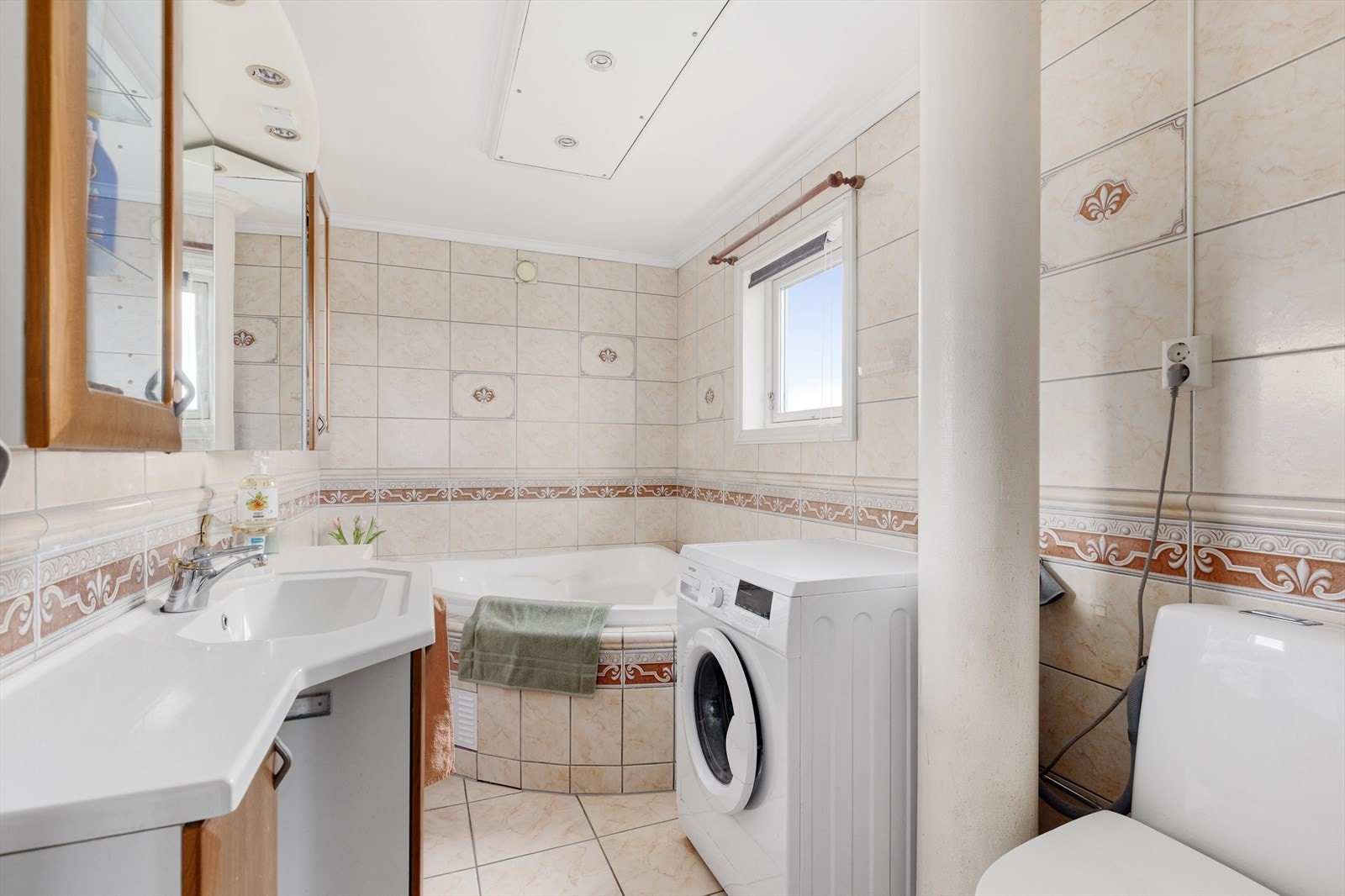 Helfliset bad med varmekabler i gulv og spotter i tak. Badet er innredet med toalett, badekar, servantinnredning og opplegg for vaskemaskin. Galleribilde