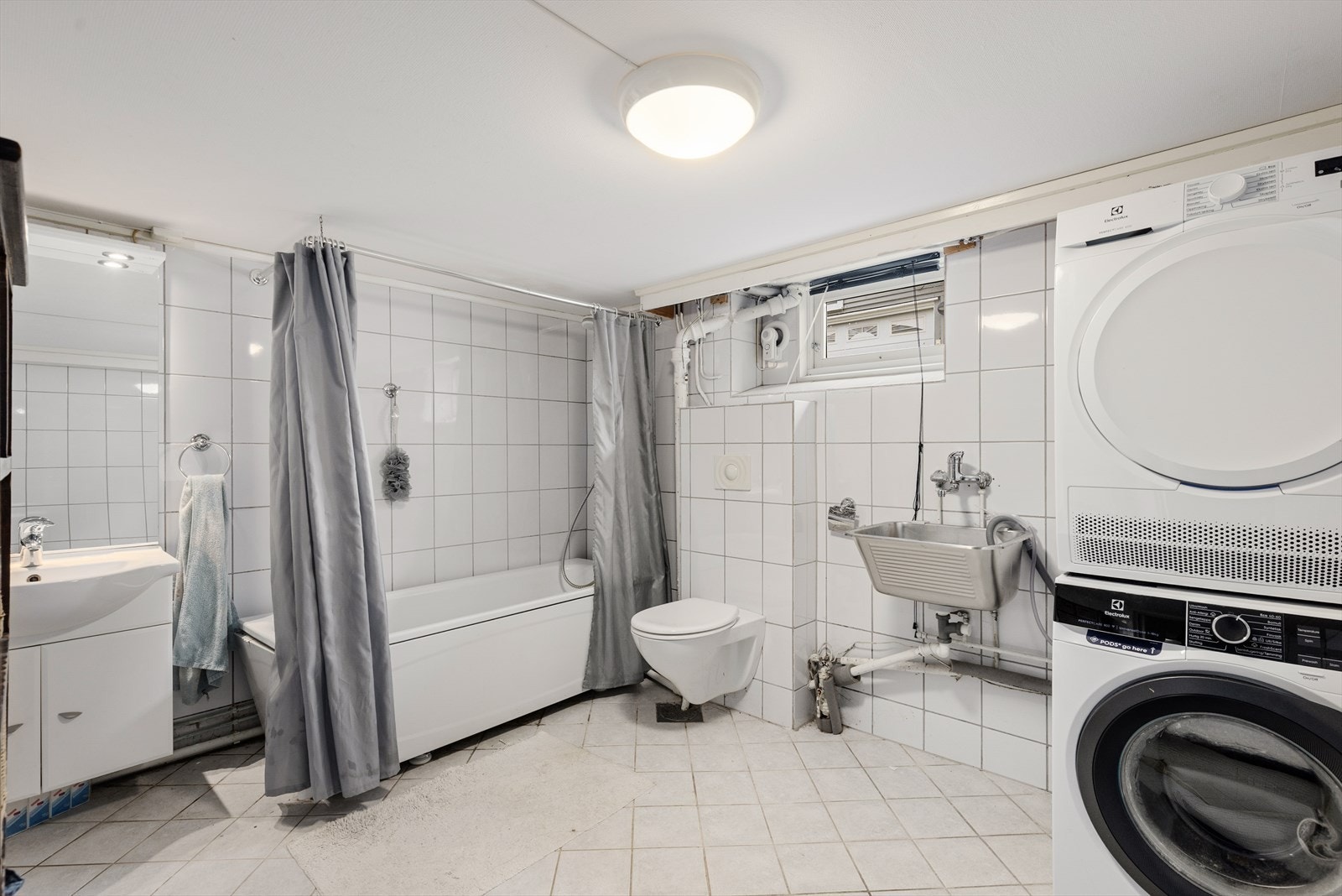 Flislagt bad med varmekabler i gulv. Badet er innredet med vegghengt toalett, servantskap, badekar og opplegg for vaskemaskin. Galleribilde