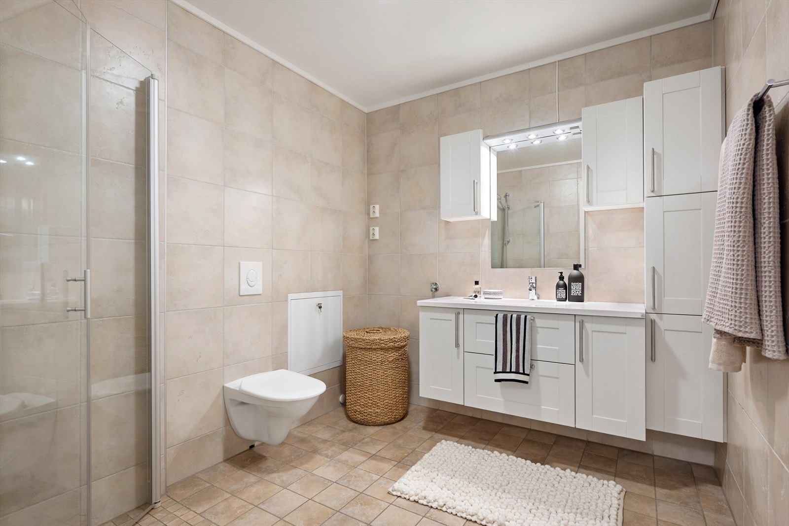 Badet er helfliset med fliser på både gulv og vegger, og har et tidløst uttrykk. Det er varmekabler i gulvet. Rommet er innredet med servantskap med nedfelt servant, speil med belysning over samt tilhørende sideskap som gir godt med oppbevaringsplass. Galleribilde