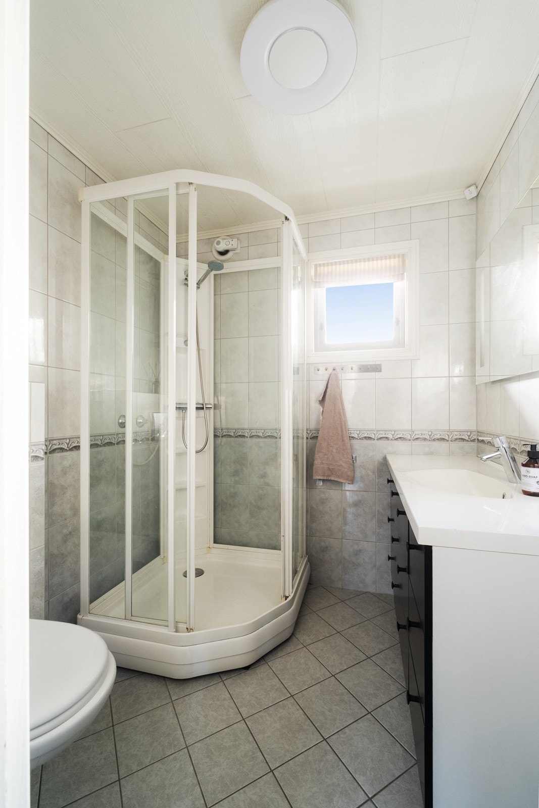 Flislagt bad utstyrt med vegghengt wc, dusjkabinett og baderomsinnredning med helstøpt servant og underskap med glatte, sorte fronter. Galleribilde