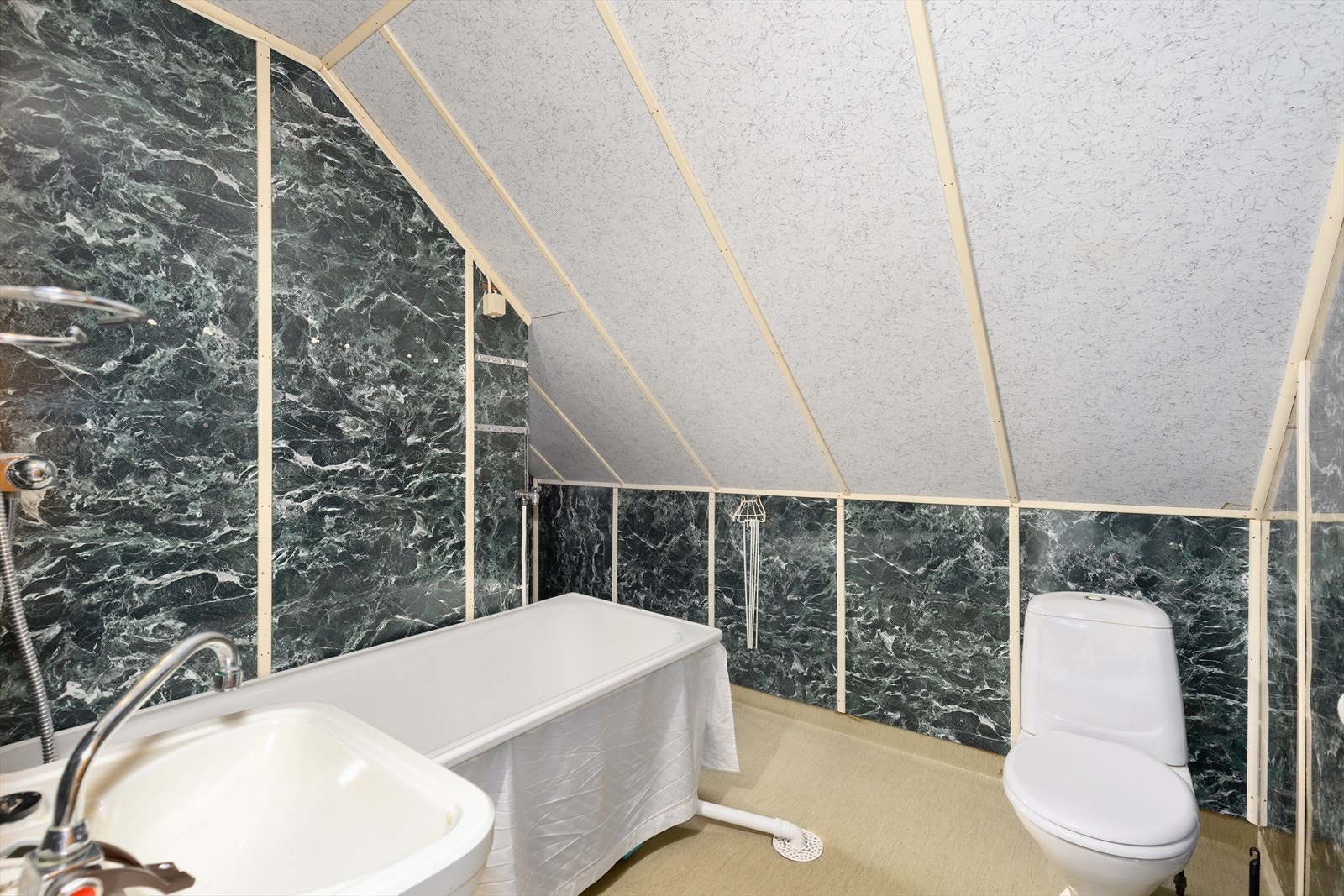 Eldre bad med belegg på gulv og baderomsplater på vegger. Her er det vask, toalett og badekar med dusj. Varme via varmelist og ventilasjon via ventil i vegg. Galleribilde