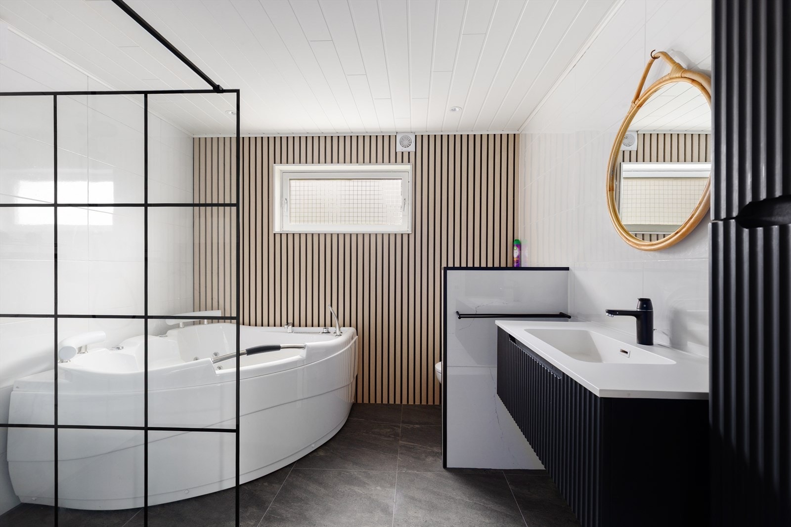 Lekkert bad fra 2024 med flis på gulv og flis/MDF-panel på vegger. Her er det dusj på vegg, boblekar, vegghengt toalett og innredning med heldekkende hvit vask og underskuff med profilert front. I tillegg høyskap med ekstra oppbevaringsplass. Galleribilde