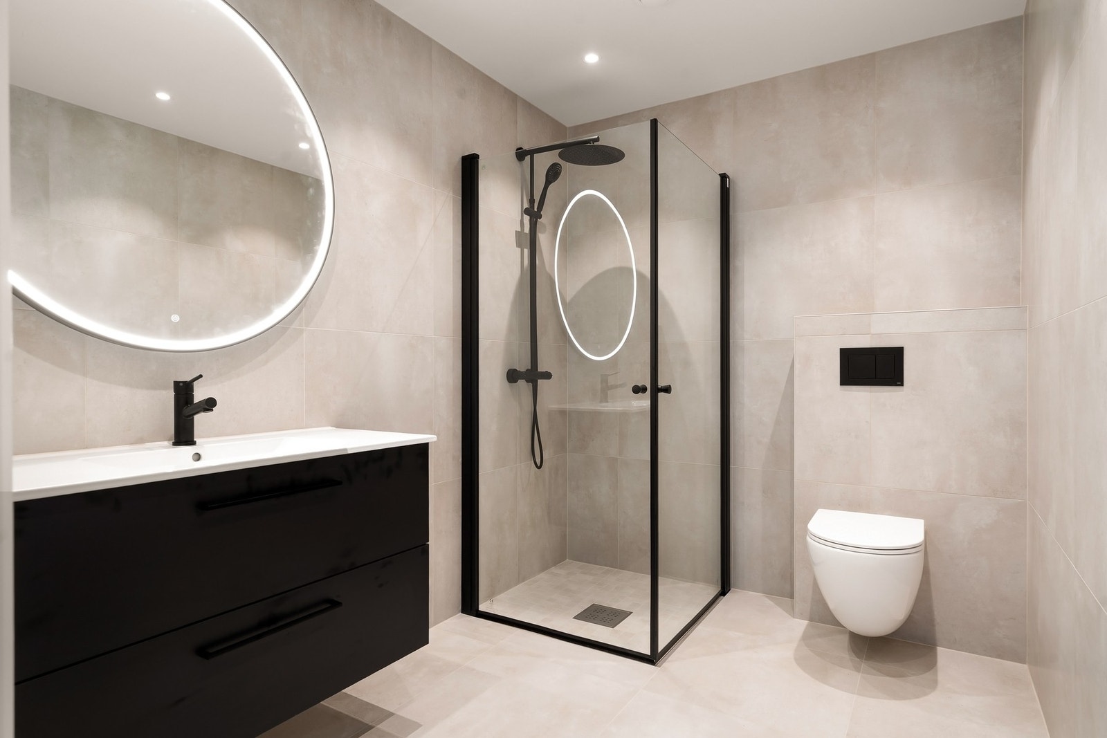 Stilig bad med dusjhjørne, vegghengt toalett, servant med skuffer og speil med lys. Galleribilde