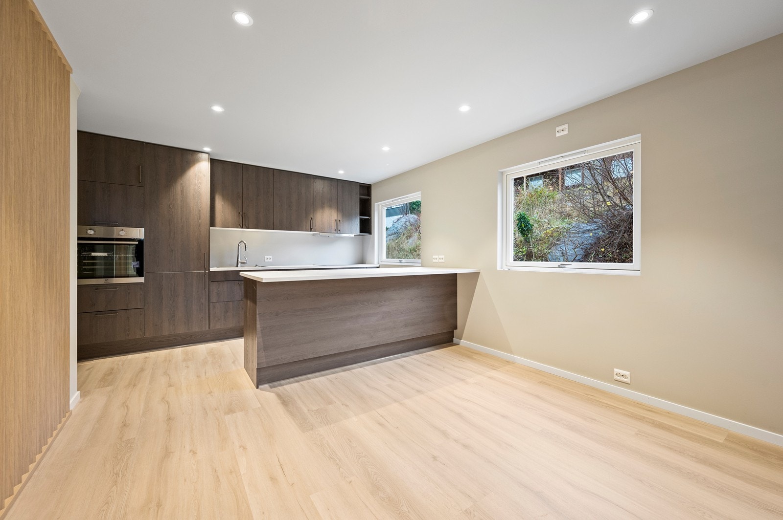 Skap og skuffer i glatte fronter. Det er en laminat benkeplate med nedfelt vask og induksjonstopp. Kjøkkenet er utstyrt med komfyr, oppvaskmaskin og kjøle- og fryseskap Galleribilde