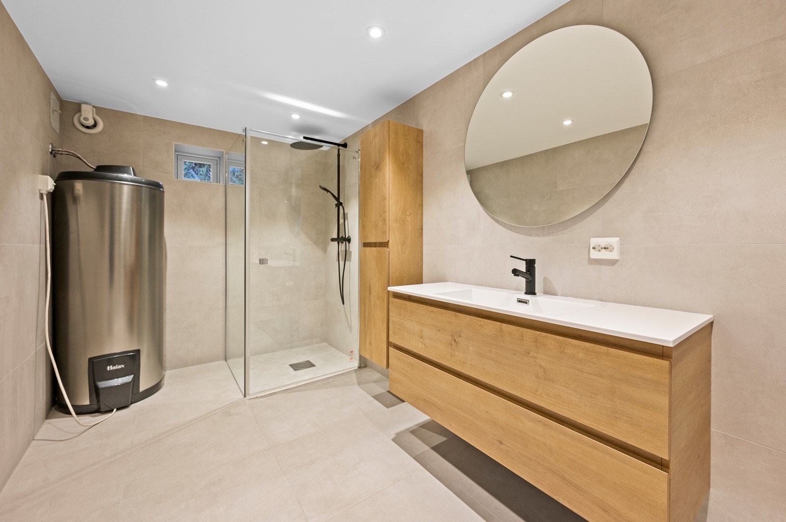 Bad i underetasje med lys baderomsinnredning. Heldekkende servantplaten med ett armatur. Speil med belysning. Veggmontert dusj med glassvegger, veggmontert toalett og opplegg for vaskemaskin Galleribilde