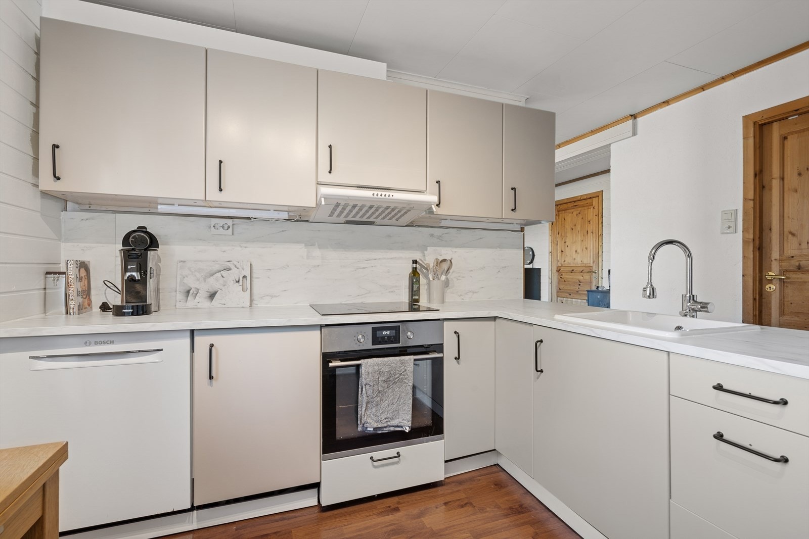 Kjøkken innredet med folierte skrog med slette fronter og laminert benkeplate. Plater på vegg over benkeplate. Galleribilde