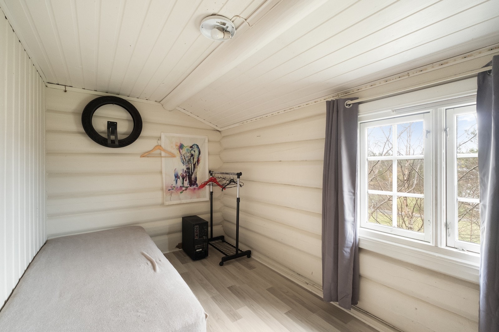 Soverom med tømmer- og panelte vegger. Vinduet gir utsikt mot hagen utenfor. Galleribilde