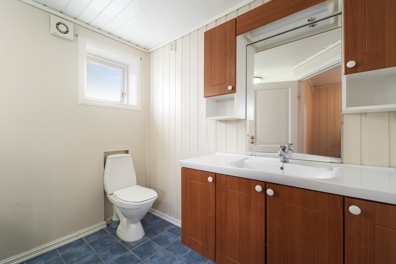 Bad med flislagt gulv og panelte og tapetserte vegger. Baderomsinnredning med heldekkende servant, over- og underskap. Galleribilde