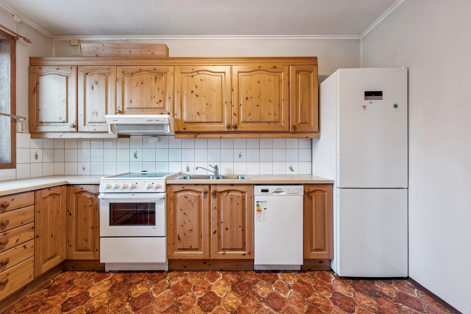 Separat kjøkken med furuinnredning, profilerte fronter og fliser over benkeplaten. Galleribilde