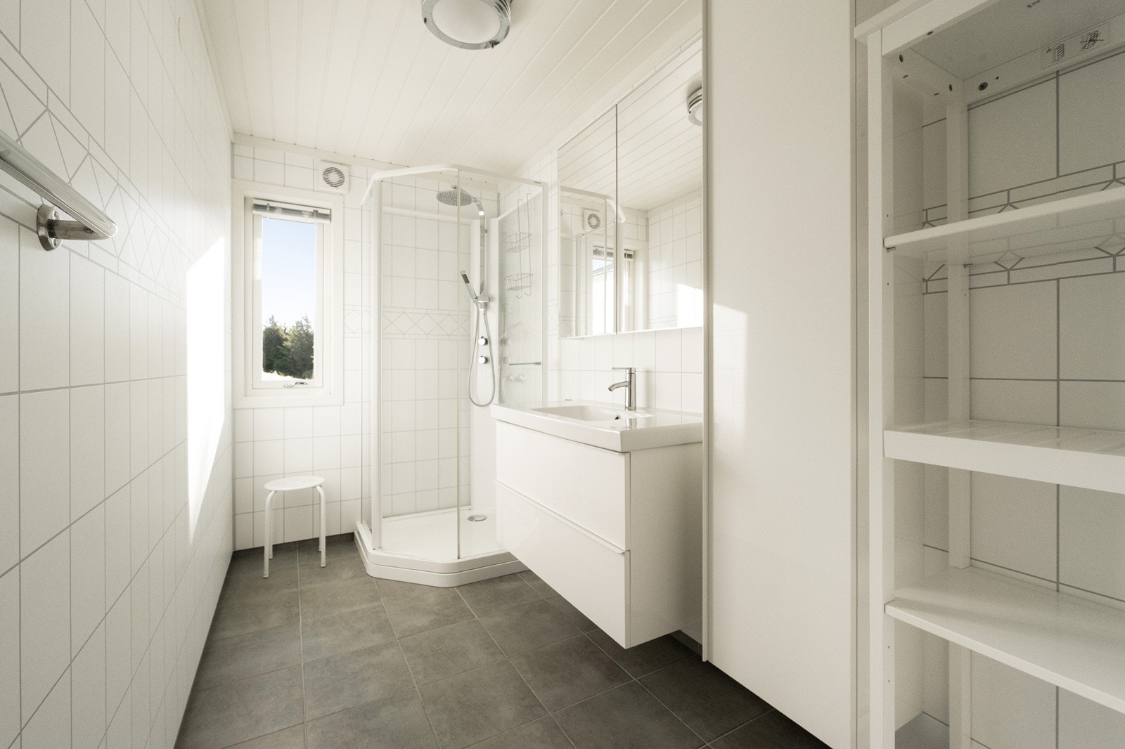 Flislagt bad innredet i tidløs stil, med heldekkende servant med underskap, høyskap, speilskap og dusjkabinett. Galleribilde