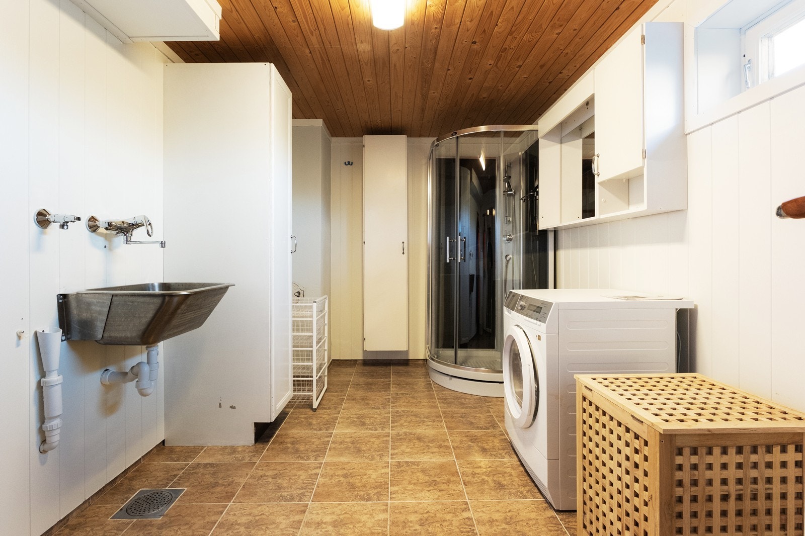 Stort vaskerom utstyrt med opplegg til vaskemaskin, utslagsvask, dusjkabinett, høyskap og veggskap. Galleribilde