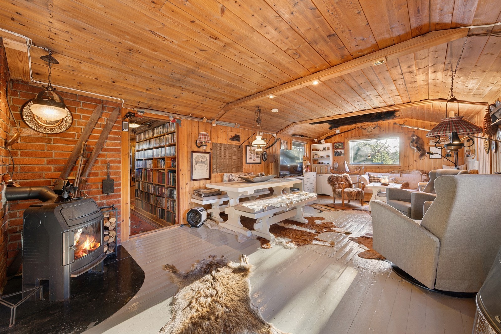 Stuen har en lun og autentisk hyttestemning, og det store bjørneskinnet montert i taket gir rommet et særpreget og rustikt uttrykk. Foran peisovnen ligger villsvinskinnet Galleribilde