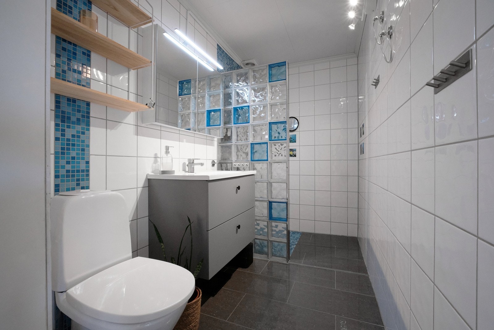 Flislagt bad utstyrt med dusjhjørne, wc, heldekkende servant, under- og speilskap. Galleribilde