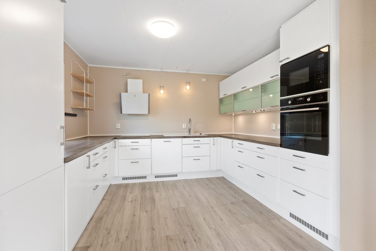 Pent kjøkken med hvite, glatte fronter. Utstyrt med kjøleskap, induksjonstopp, mikrobølgeovn og stekeovn. Galleribilde