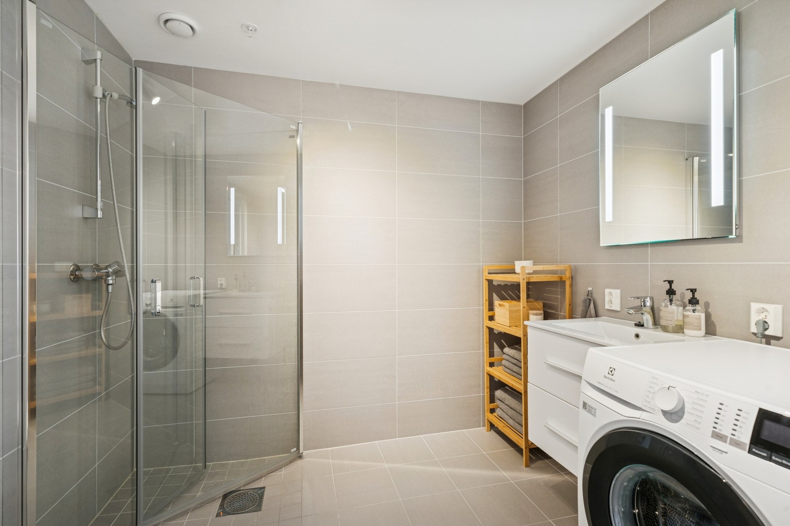 Badet er videre utstyrt med en hvit baderomsinnredning, bestående av vegghengt skuffeseksjon, heldekkende servant og et speil med integrert belysning. Galleribilde