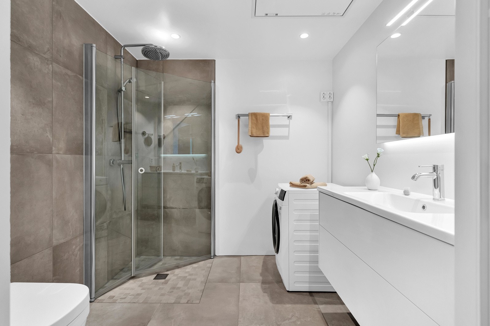 Delikat, flislagt bad med opplegg for vaskemaskin og dusjhjørne med innfellbare dører. Vaskemaskinen medfølger salget Galleribilde
