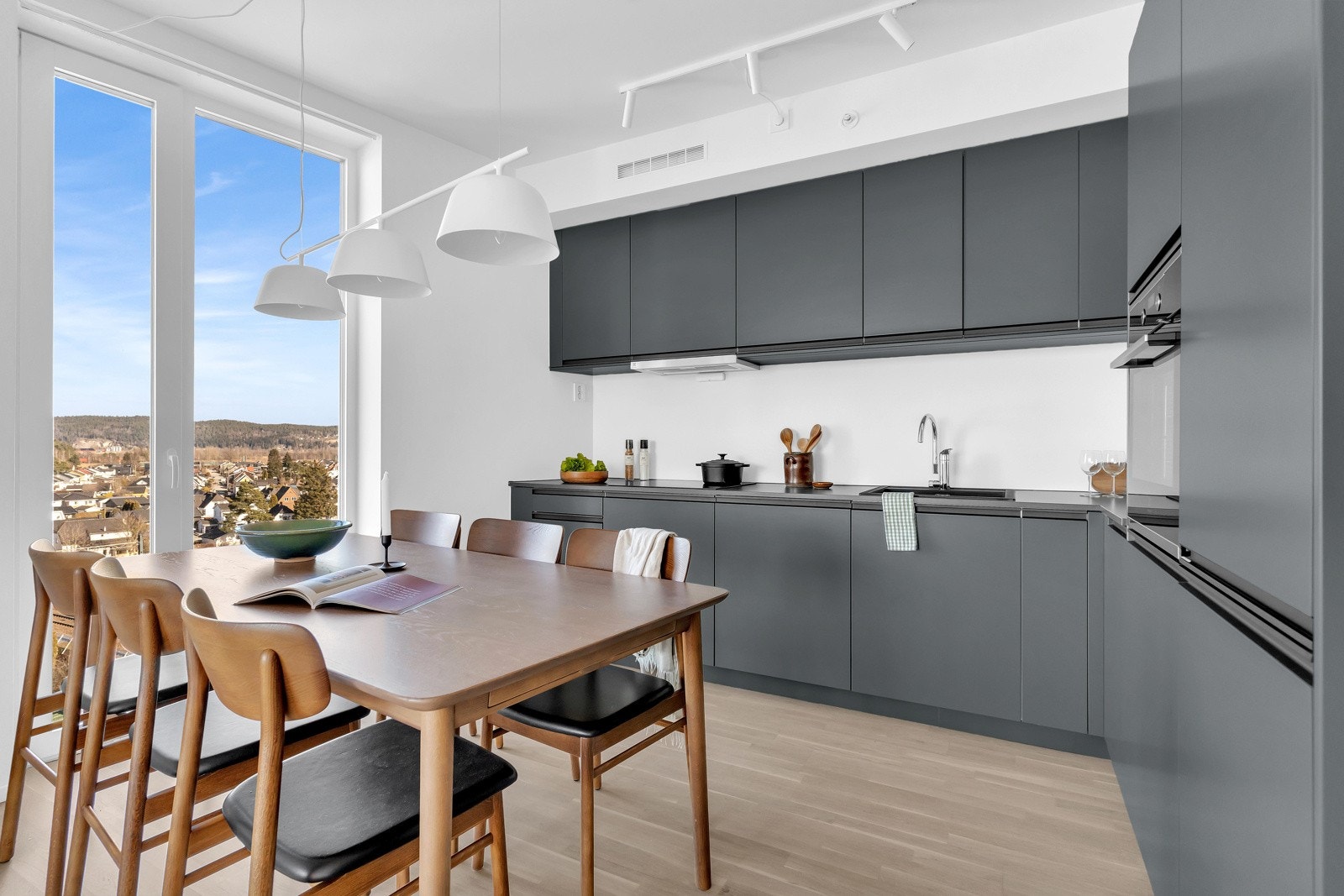 Kjøkkeninnredningen har mørke fronter med takhøy innredning, benkeplate i laminat og integrerte hvitevarer Galleribilde