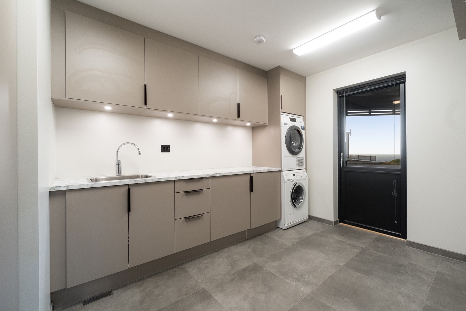 Praktisk vaskerom med vaskeromsinnredning, vaskekum, benkeplate og egen dør ut. Galleribilde