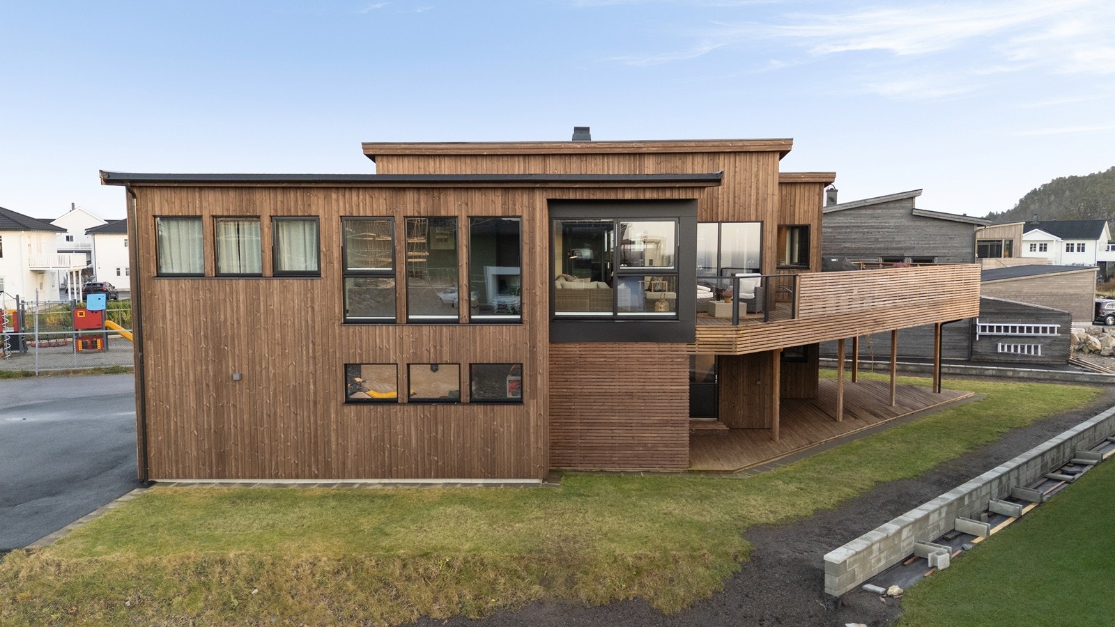 Fasade vest med store vindusflater, stående trekledning og platefelt. Galleribilde