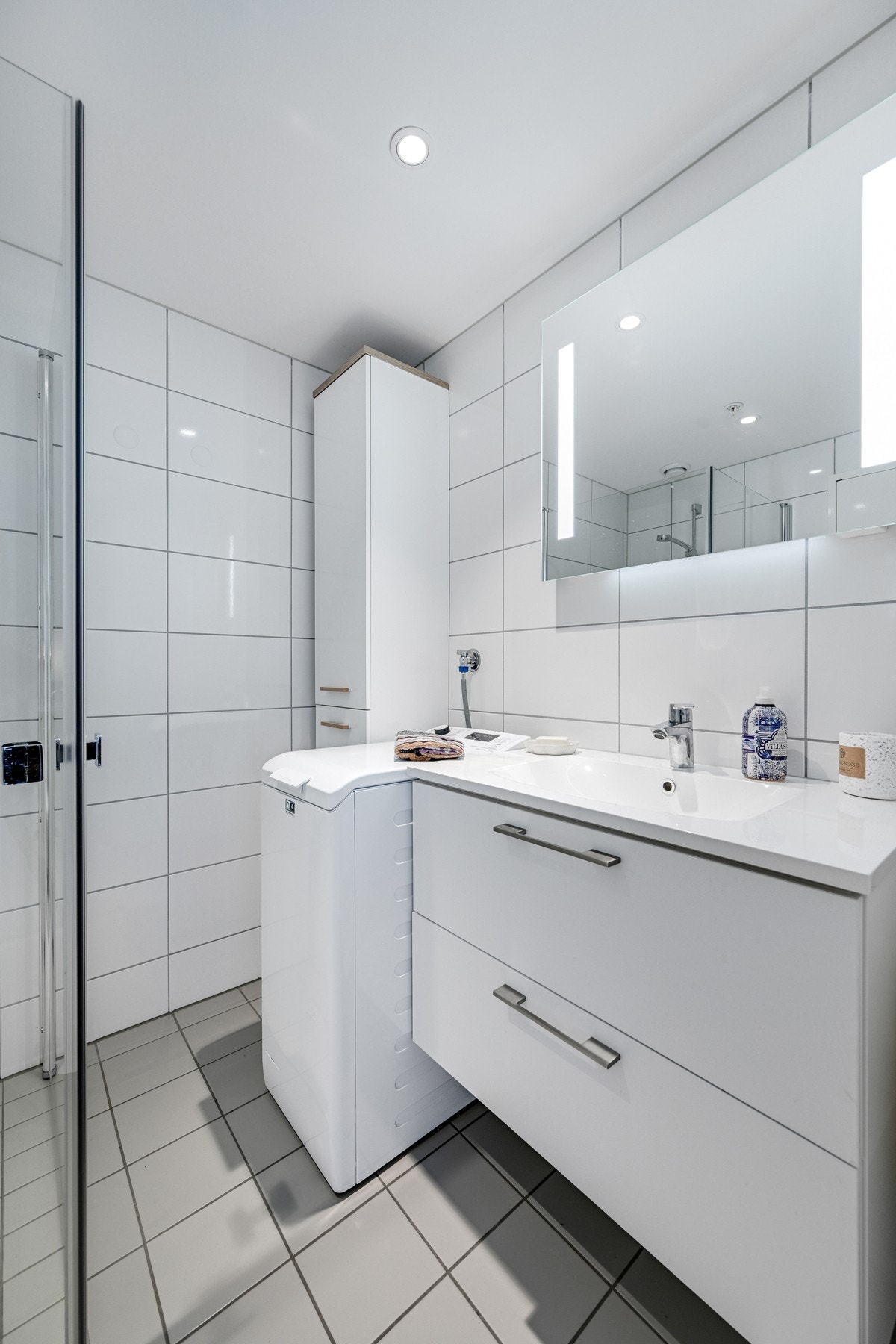 Badet inneholder servant, speil med lys, høyskap, dusjhjørne, vegghengt wc og opplegg for vaskemaskin. Galleribilde