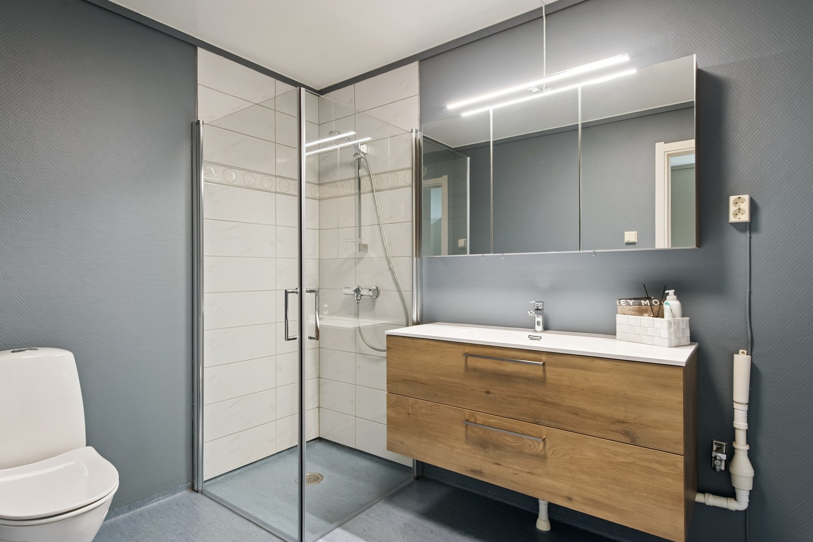 Badet har flislagt dusjsone med innfellbare glassdører og vinylbelegg på gulv. Galleribilde