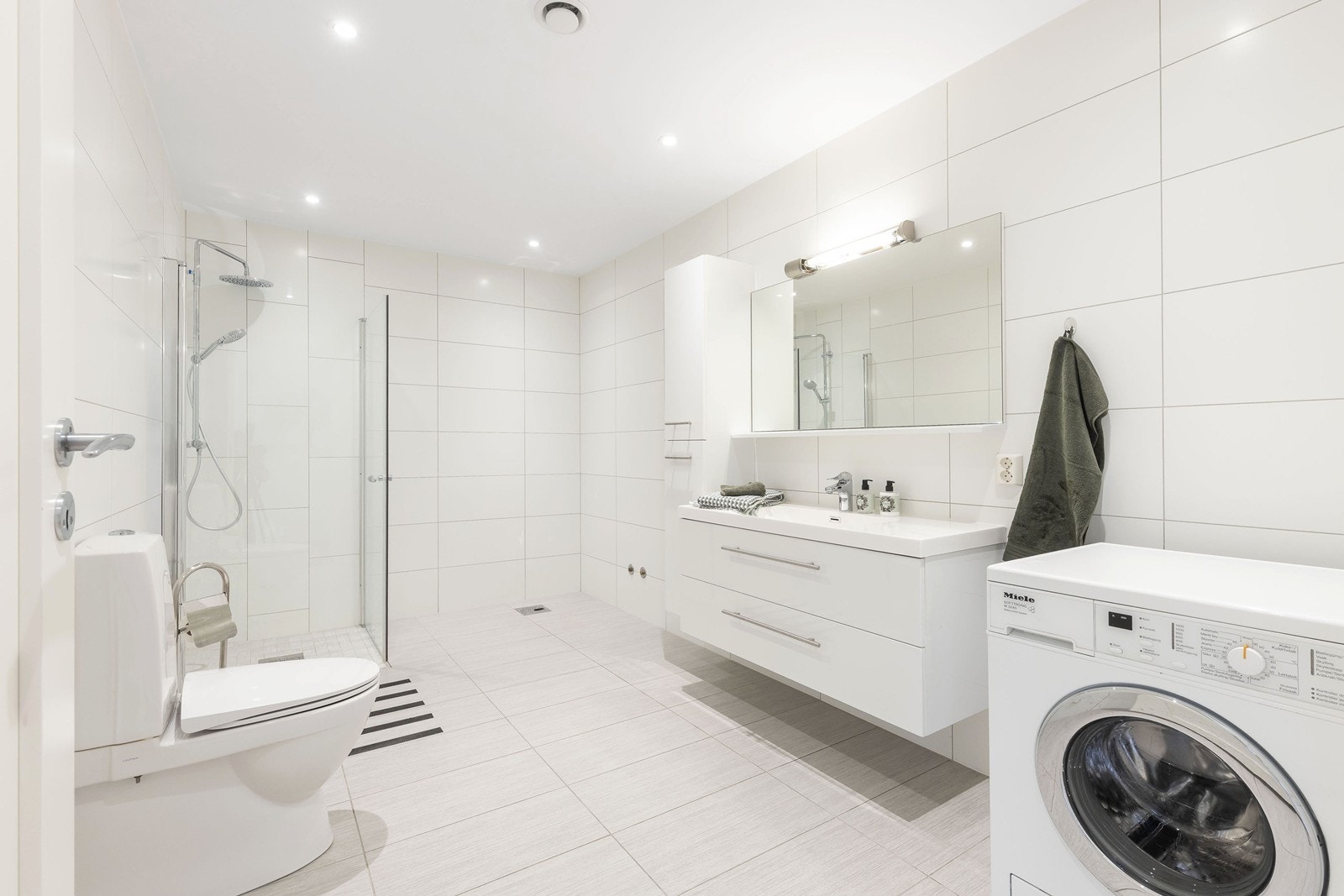 Stort flislagt bad med dusjhjørne og opplegg til vaskemaskin Galleribilde