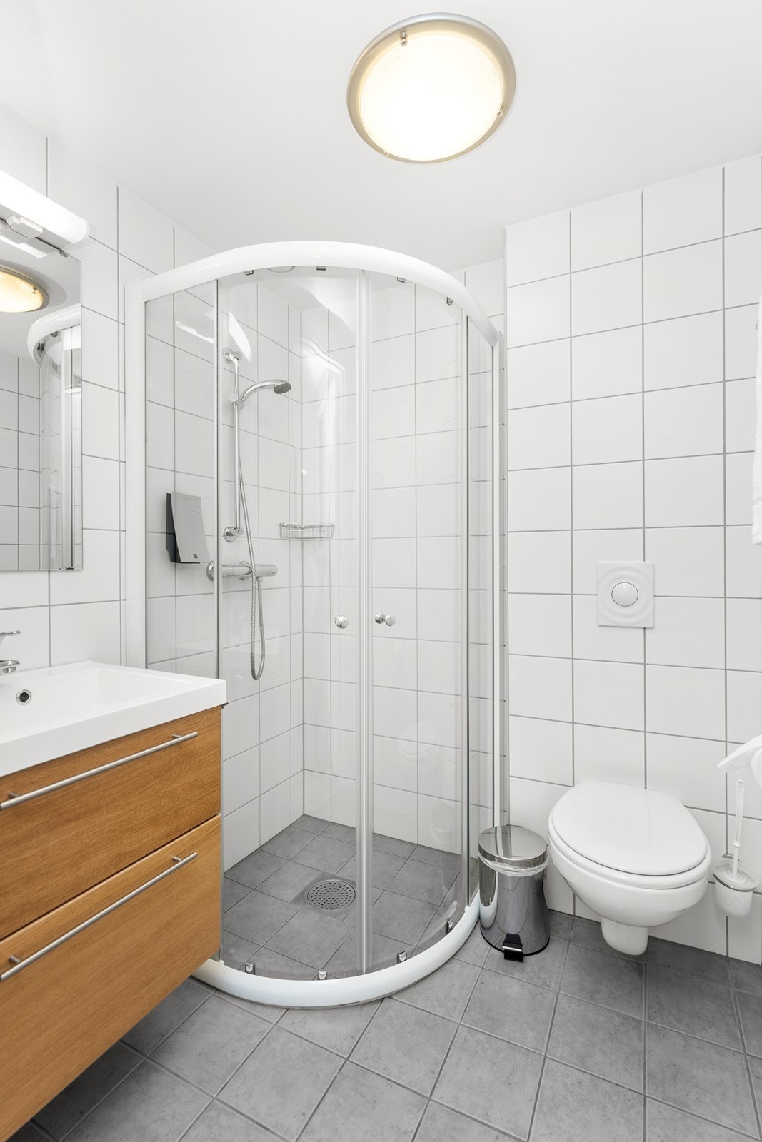 Bad på hotellrom har flislagt gulv og vegger. Vegghengt toalett, dusjhjørne og innredning med nedfelt servant. Galleribilde