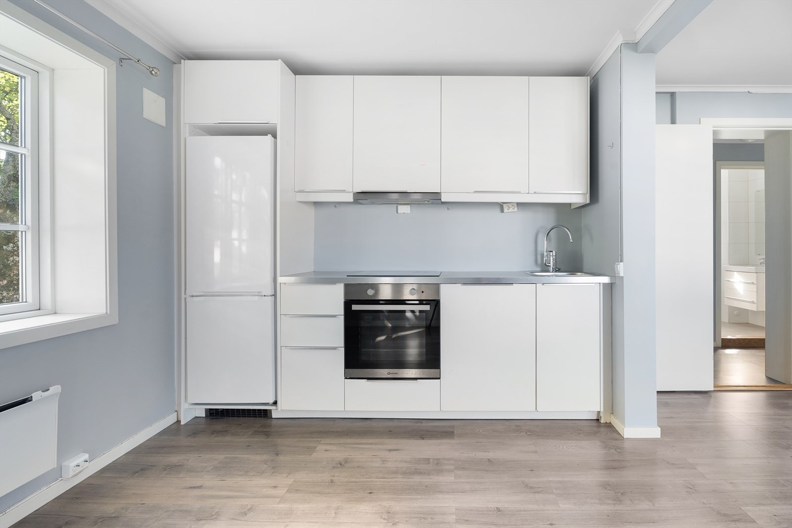 Tidløs kjøkkenløsning med innredning fra IKEA med glatte fronter og benkeplate i laminat. Kjøkkenet er utstyrt med integrert stekeovn, koketopp og oppvaskmaskin. Plass for kjøl/frys. Galleribilde