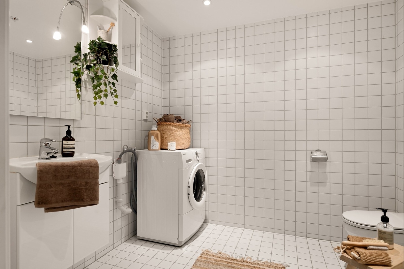 Romslig bad med fliser på både gulv og vegger med opplegg for vaskemaskin og vegghengt wc Galleribilde