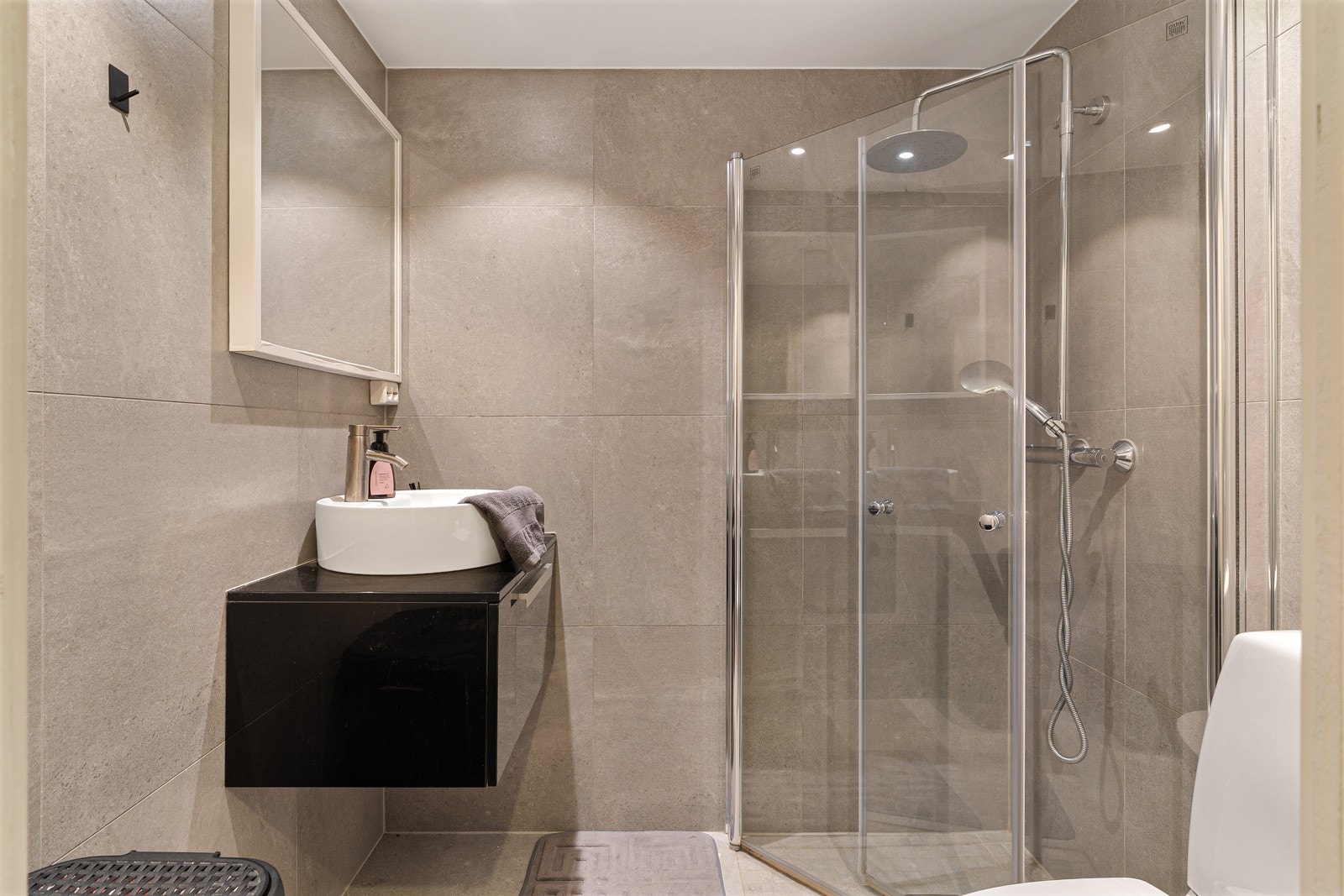 Lyst flislagt bad på hybelavdelingen med sort innredning med speil, servant og praktiske dusjdører. Galleribilde