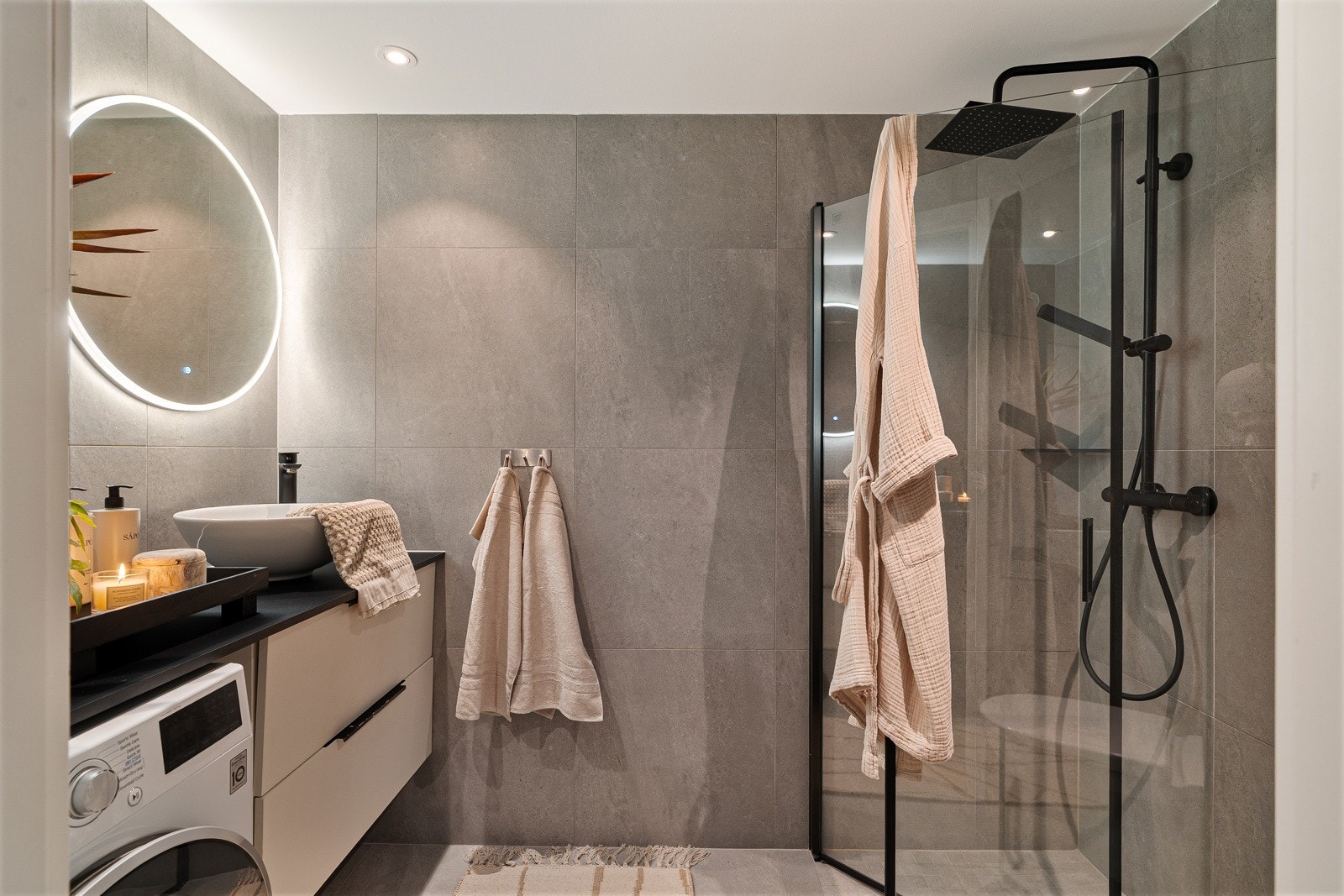 Delikat flislagt baderom med varmekabler i gulv og praktiske dusjvegger. Badet har servant, med en skuffer i innredningen, speil med led-lys og downlights i himling. Galleribilde