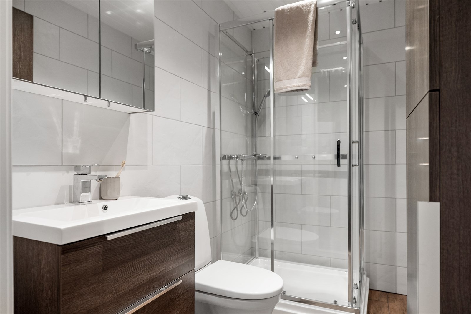 Baderommet er innredet med elegant dusjkabinett, toalett og møbler i valnøttfarge, samt vannbåren gulvvarme. Galleribilde