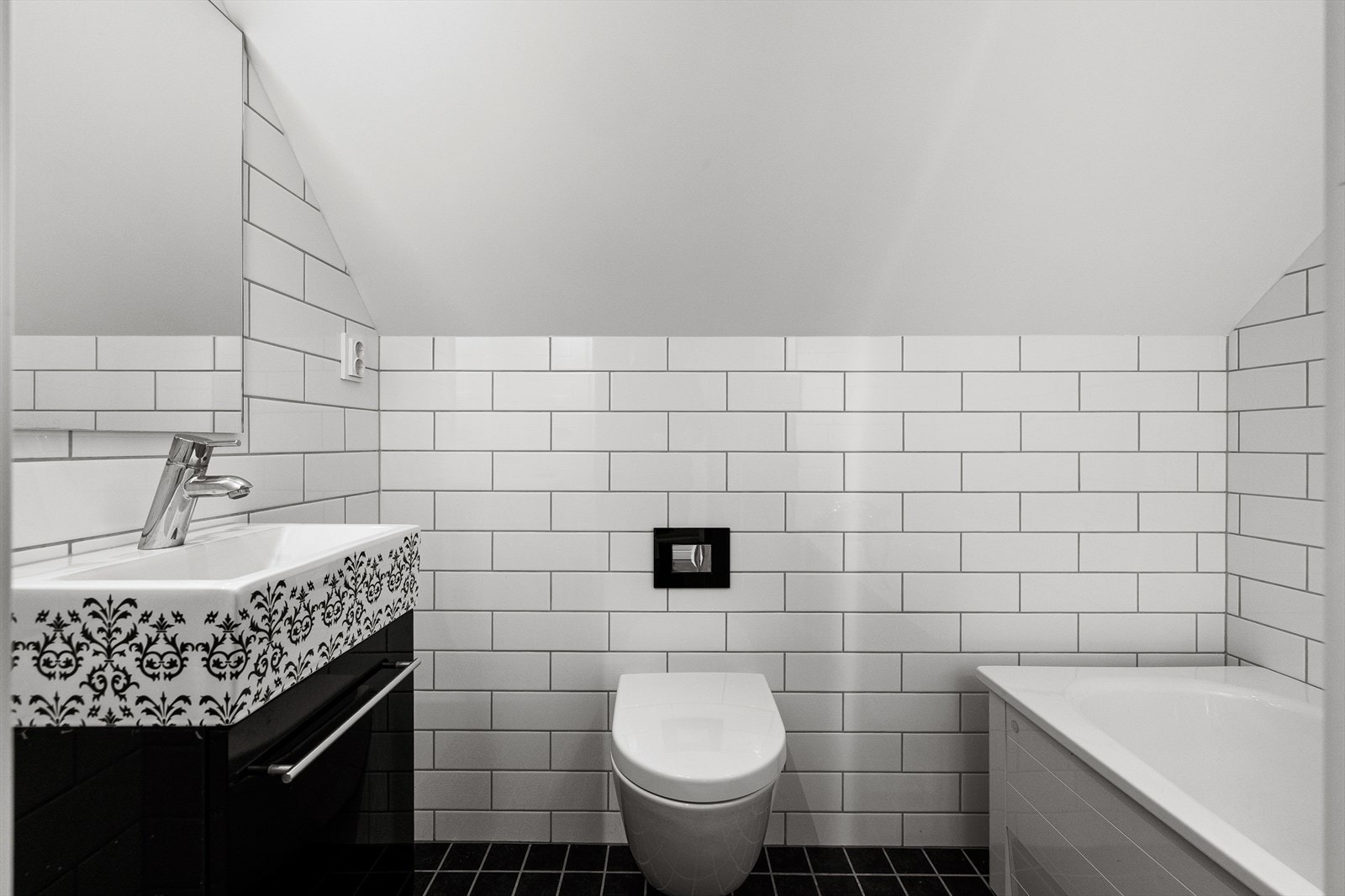 Lekkert, kompakt bad i kontinental stil, med svarte gulvfliser og hvite metrofliser på veggene. Galleribilde