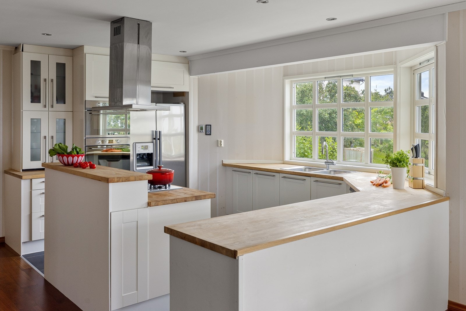 Stort, lyst kjøkken med karnappvindu langs veggen med benk og vask. Galleribilde