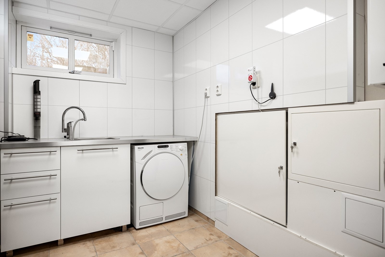 Eget vaskerom/teknisk rom med innredning med stålbenk, vaskekum, skuffer og skap. Opplegg til vaskemaskin. Galleribilde