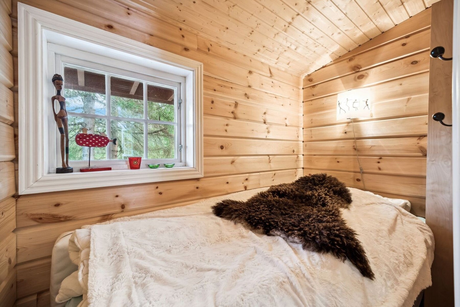 Sjarmerende rom med lune trevegger og myke tekstiler. Rommet er innredet med en komfortabel seng, og vinduet slipper inn naturlig lys med utsikt mot skogen. Galleribilde