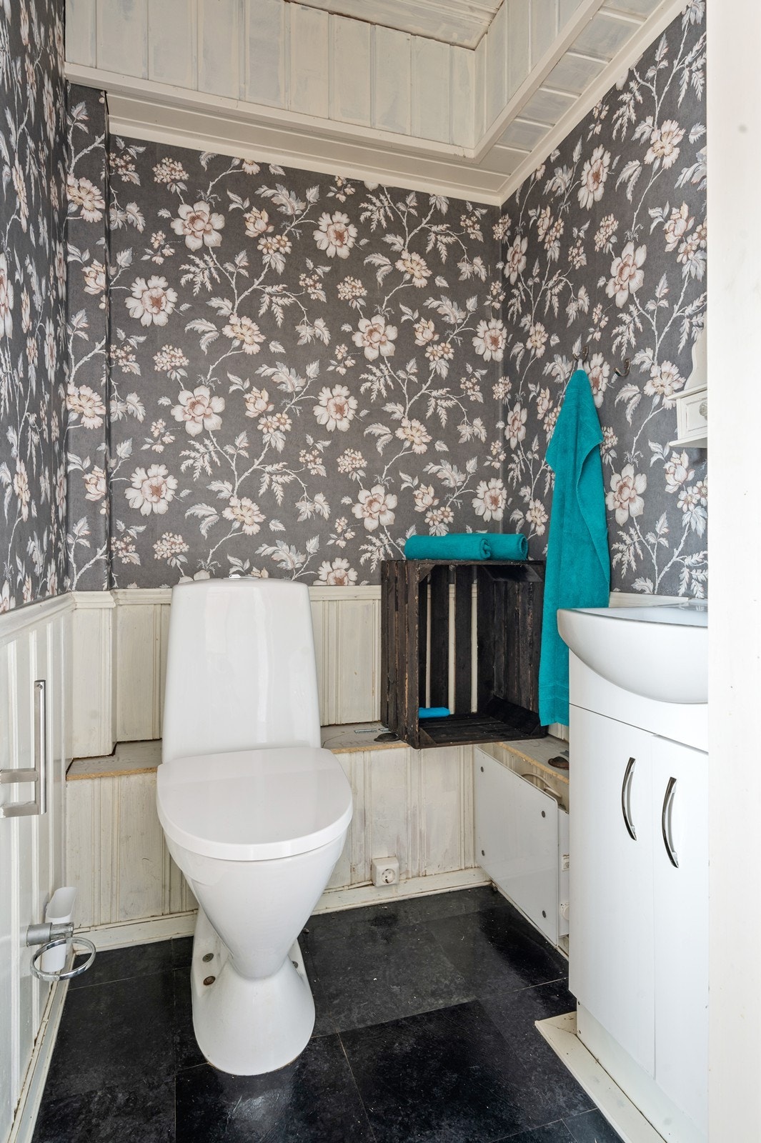 Separat toalettrom med laminat på gulvet og dels malt trepanel og dels tapet på veggene. Rommet er utstyrt med gulvmontert wc og servant i skapinnredning Galleribilde