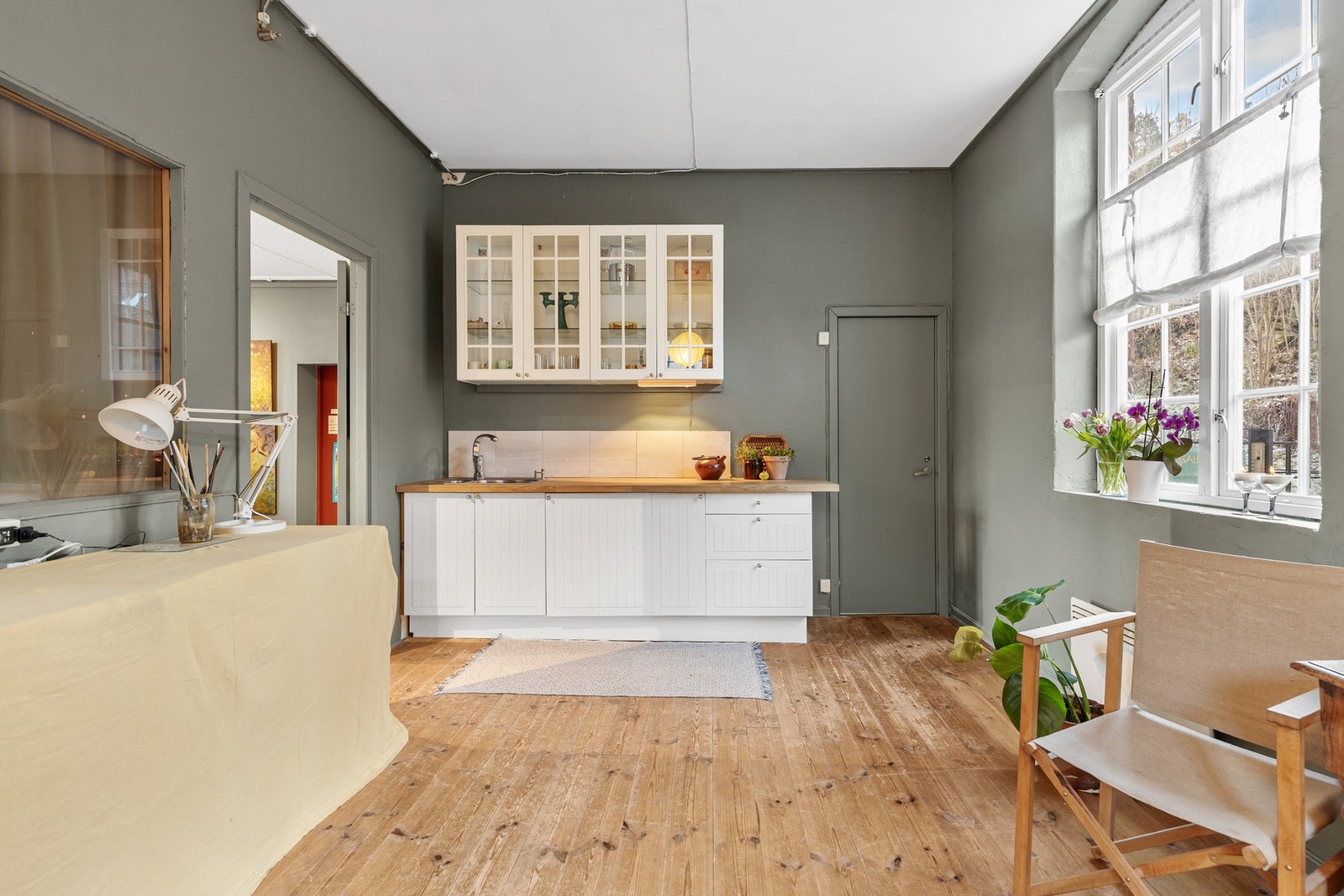 I det ene hjørnet er det montert en enkel kjøkkeninnredning med hvite, profilerte fronter og benkeplate av laminat med vaskekum Galleribilde