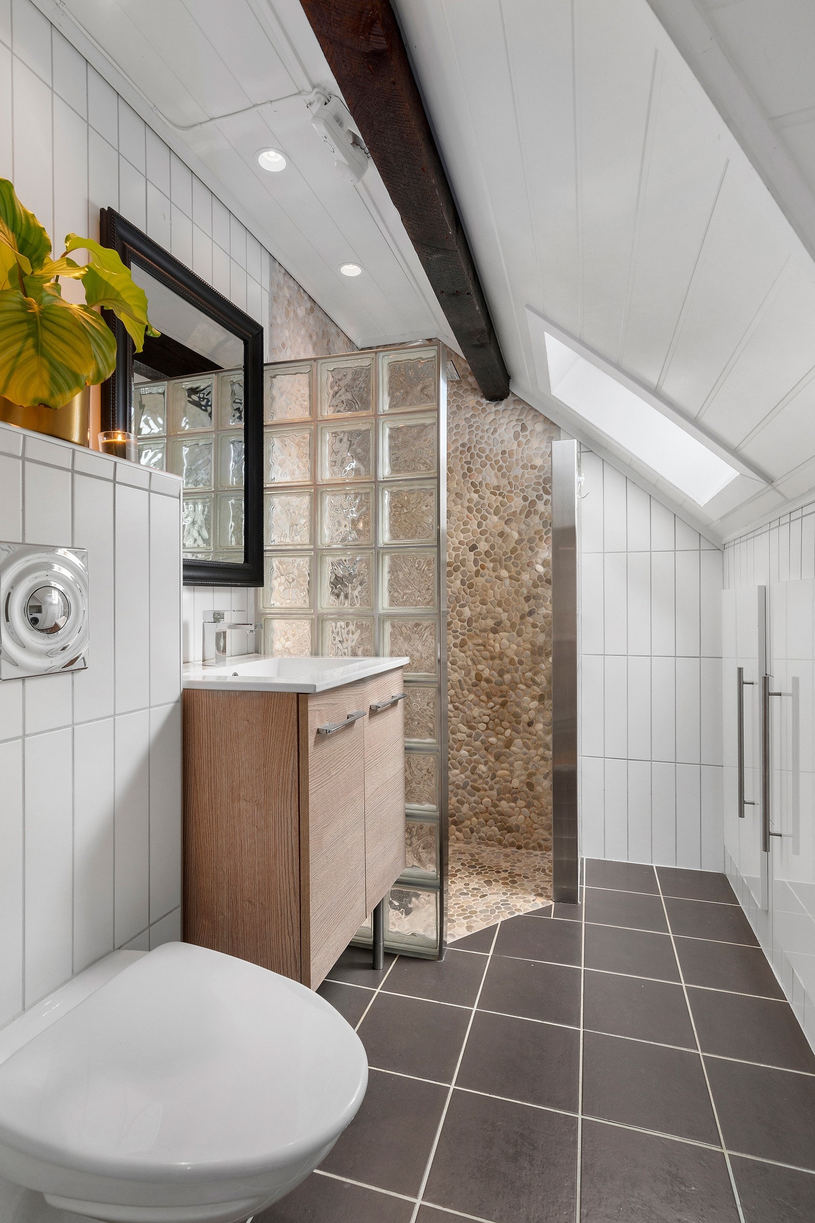 Badet har fliser på gulv og vegger, mens det i dusjsonen er lagt rullesteiner. Pen innredning med servant, med speil over. Galleribilde