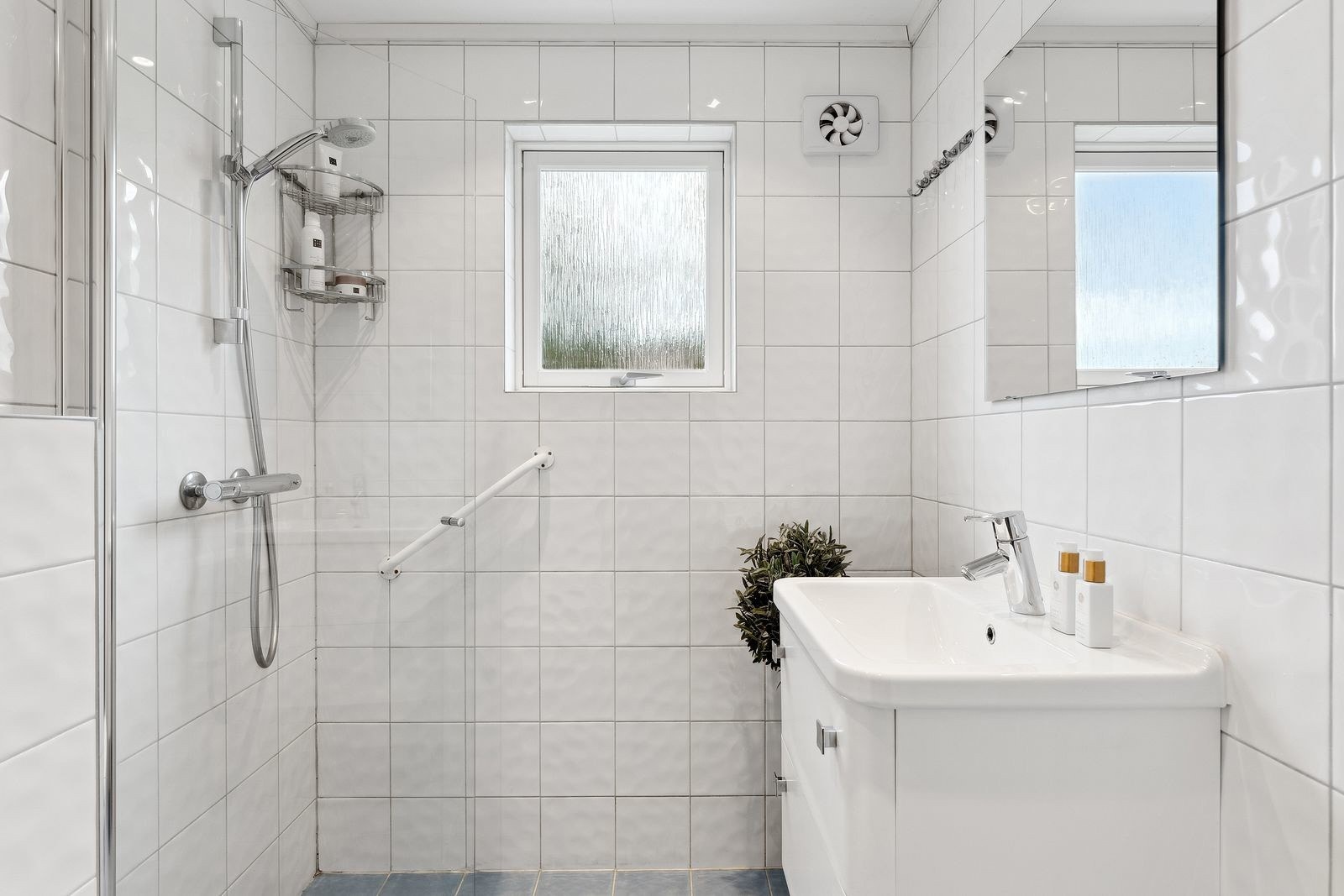 Delikat, flislagt bad innredet med med dusjhjørne, servant i innredning, veggspeil og vegghengt toalett. Galleribilde